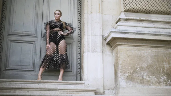 階段の上の歴史的な建物に立っている黒点線の透明なドレスと下着で驚くべきセクシーなブロンドプラスサイズモデルとポージング。行動だ。体正の概念. — ストック写真