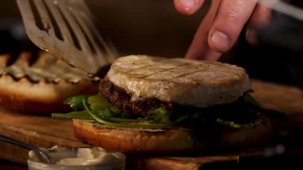 Close up of male hands putting camembert cheese on homemade hamburger with sauce and greenery, foodporn concept. Stock footage. Preparation of fat tasty burger. — ストック動画