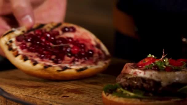 Κοντινό πλάνο του σάντουιτς χάμπουργκερ με κοτολέτες κιμά, τυρί μπρι, καμαμπέρ, σάλτσα κεράσι μούρο. Στικ. Αρσενικό σεφ βάζοντας top burger bun στα άλλα συστατικά, foodporn και fast food — Αρχείο Βίντεο