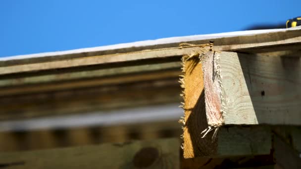 Gros plan de la construction en bois de toiture avec un clou et une corde serrée autour sur fond bleu ciel. Images d'archives. Planches de bois rugueuses et couverture de toit tissu blanc oscillant dans le vent . — Video