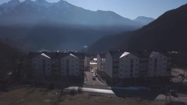 Vue aérienne de la petite ville située dans la vallée entourée de hautes montagnes couvertes d'arbres. Clip. Voler au-dessus de la ville près des collines boisées sur fond de ciel bleu . — Video