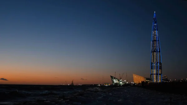 Uitzicht op de wolkenkrabber bij de rivier in de avond. Concept. Prachtige moderne wolkenkrabber aan de oever van de baai in de avond — Stockfoto