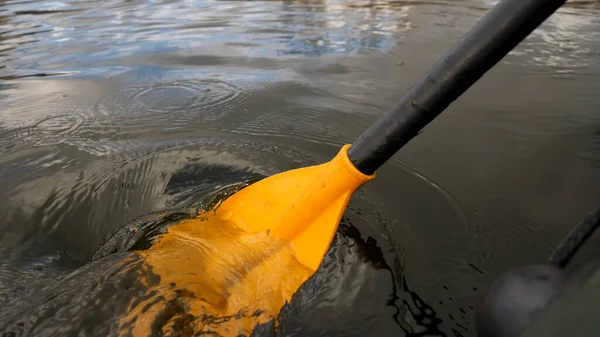 Close up de um homem em um rio em um barco de borracha verde com uma pá amarela. Imagens de stock. Remo masculino com um remo sentado em um barco de borracha . — Fotografia de Stock