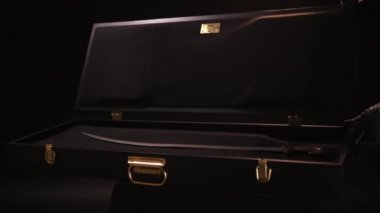 Close up of ancient valuable sward lying inside of wooden case with gold clasps. Stock footage. Hands in leather gloves open beautiful case with the antique exhibit, steel sabre inside.