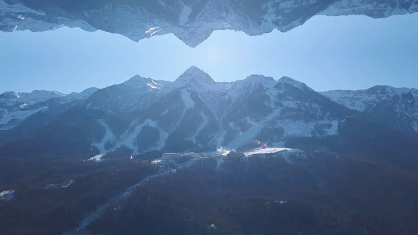Breathtaking landscape of snowy mountains with mirror reflection effect. Clip. High hills covered by forest in winter season and the ski resort, inception theme. — Stock Fotó