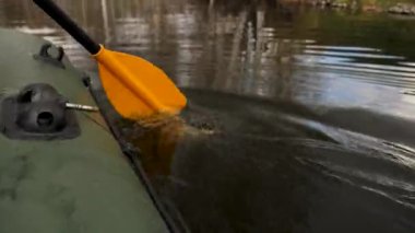 Close up of a man on a river in a green rubber boat with a yellow paddle. Stock footage. Male rowing with an oar sitting in a rubber boat.