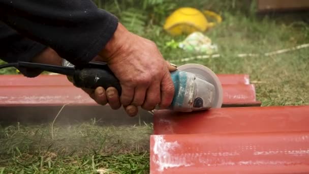 Roofer usando uma máquina de moedor de ângulo para cortar uma telha de telhado de cor vermelha. Imagens de stock. Close up de mãos de trabalhador do sexo masculino cortando uma telha do telhado com uma serra profissional . — Vídeo de Stock