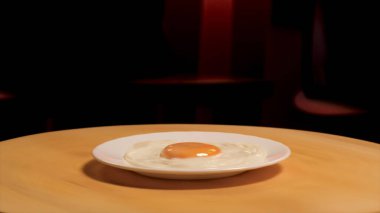 Fried egg on a plate rotating on a wooden board on dark room background. Stock footage. Close up of white glass plate with fried egg on it.