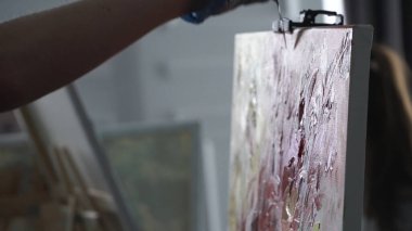 Art painting with palette knife. Stock footage. Side view of an artist hand in latex glove using professional palette knife for creating a masterpiece.