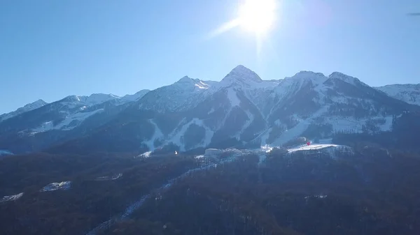 Vista aérea da estância de esqui durante um dia vibrante de inverno. Clipe. Voando sobre as montanhas cobertas de neve no céu azul claro com sol brilhante . — Fotografia de Stock