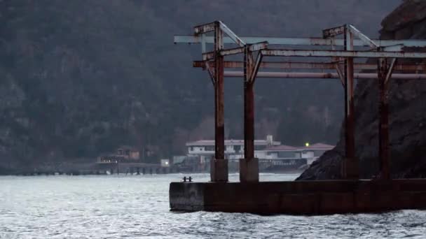 Kayalık sahildeki Rusty Pier. Vuruldu. Kayalık sahildeki balıkçı teknesinin arka planında bulutlu havada eski gemiler iskelesi boş. Bulutlu havada kayalıklardaki paslı iskele seni üzüyor. — Stok video