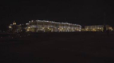 Saint Petersburg şehir merkezinin manzaralı, aydınlık mimarisi, görkemli Kış Sarayı. Etrafta insanlar geziniyor. Hareket. Kara gökyüzü arka planında ünlü Hermitage binası.