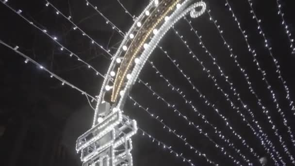 Vista inferior de la ciudad nocturna en Navidad, guirnaldas y arco brillante sobre fondo de cielo negro. Moción. Decoraciones de la ciudad antes de las vacaciones de Año Nuevo . — Vídeo de stock