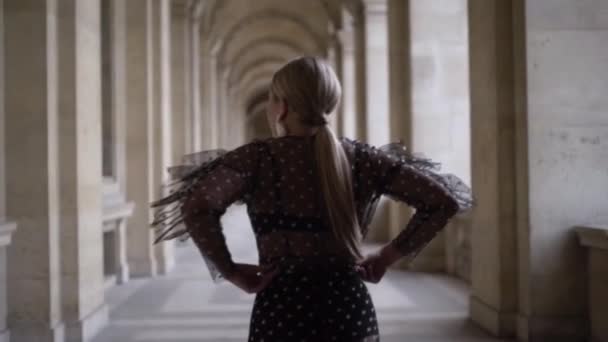 Vue arrière d'une jeune femme tirant vers le haut de sa robe tout en se tenant près du bâtiment historique. L'action. Jolie jeune femme en tenue à la mode debout à l'extérieur . — Video