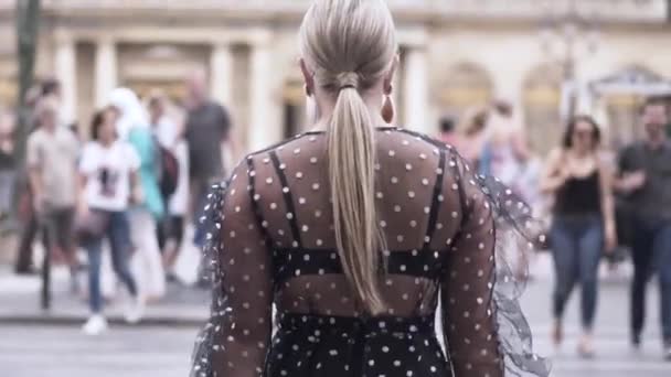 Rear view of a pretty woman in black transparent dress crossing the street near the crowd of people. Action. Sexy blond plus size model walking in a big city. — Stockvideo