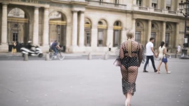 Joven mujer bonita con el pelo rubio en frente de un gran edificio histórico, Francia, viajando por Europa. Acción. Sexy dama con gasa vestido punteado caminando en la calle . — Vídeos de Stock