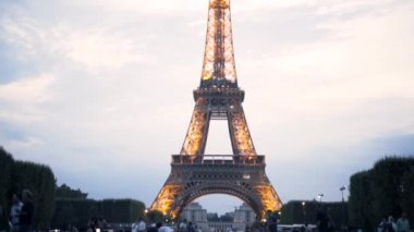 Eyfel Kulesi, Fransa ve Paris 'te mavi bulutlu arka planda parlayan ve yanıp sönen birçok lambayla dekore edilmiştir. Başla. İnsanlar ünlü manzaranın yakınındaki yeşil çayırlarda vakit geçirir..