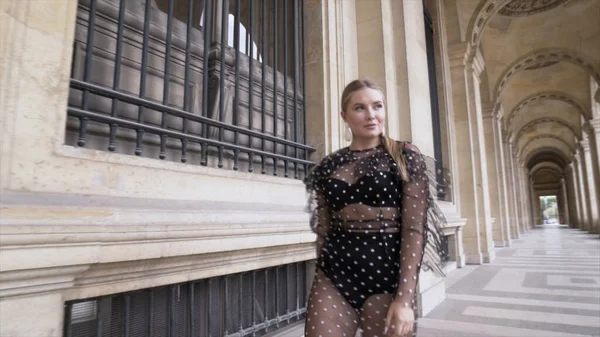 Young pretty woman with blond hair in black sexy dress and underwear walking near european historic building. Action. Attractive plus size model posing in front of the camera, body positive concept. — Stock Fotó