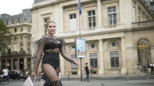 Mulher europeia elegante vestindo vestido sexy pontilhado preto e bolsa pequena branca, Paris, França. Acção. Loira plus size modelo andando na rua . — Fotografia de Stock