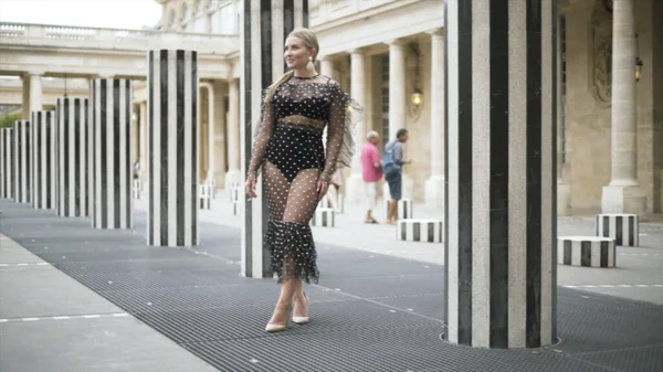Szépség lány csillogó megjelenés visel szexi átlátszó ruha és fekete fehérnemű és álló közelében csíkos oszlopok Párizsban, Franciaországban. Felvétel. Érzéki nő szőke hajjal és divatos megjelenéssel. — Stock Fotó