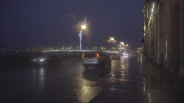 Podzimní deštivá městská ulice v noci, noční provoz na mokré silnici během deště, pouliční osvětlení odrážející se v loužích. Pohyb. Krásný nábřeží a osvětlený most, první osoba střelecký efekt. — Stock video