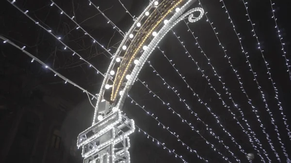 Untere Ansicht der Nacht Stadt in der Weihnachtszeit, Girlanden und leuchtenden Bogen auf schwarzem Himmel Hintergrund. Bewegung. Stadtdekoration vor dem Neujahrsfest. — Stockfoto