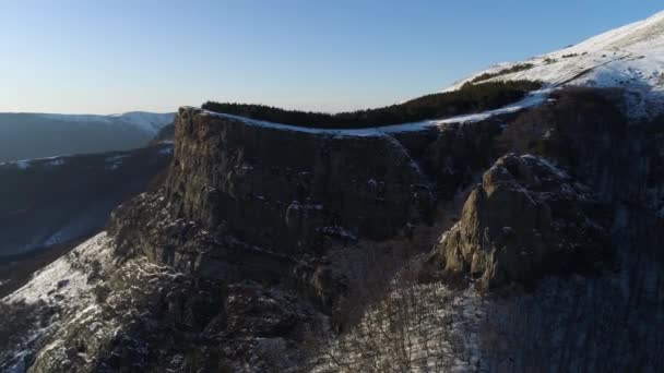 Yüksek kaya kütlesinin yamacı mavi gökyüzü arka planında çam ağaçlarıyla kaplıdır. Vuruldu. Ormandaki dağ yamacı ve karlı tepe.. — Stok video