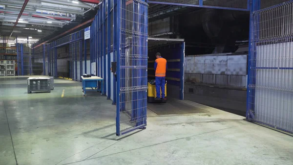 Worker on loader transports boxes in warehous. Scene. Worker standing on loader controls it to transport cargo boxes in factory warehouse