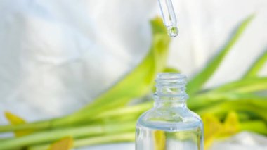 Kadının yüzü nemlendirmek için serumu yakın planda tutması. Kavram. Kadın, beyaz arka planda çiçekli yüzü nemlendiren lüks bir serum gösteriyor. Yüz yağının sıvı dokusu