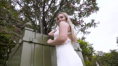 Çiçek açan ağacın yanında duran güzel beyaz elbiseli çekici sarışın bir kadının bahar portresi. Başla. Sarışın, gülümseyen bir kadının yaz günü beyaz mini elbiseli hali..