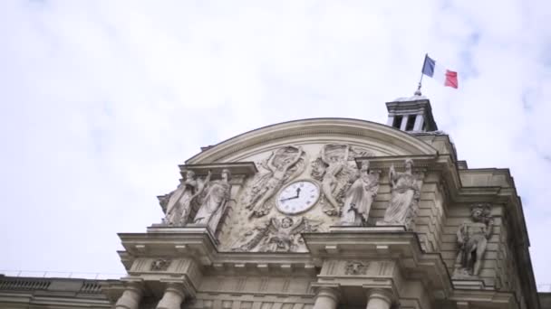 Französische Flagge weht im Wind an einem historischen Gebäude, Architekturkonzept. Handeln. Blick von unten auf einen schönen Altbau mit Skulpturen und Uhr. — Stockvideo