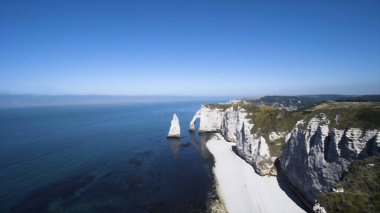 Yüksek sarp kıyılar çimlerin yeşilliği ve sonsuz mavi denizle uyum içindedir. Başla. Mavi gökyüzü arka planındaki kıyı şeridinin doğal uçurum oluşumlarının hava görüntüsü.
