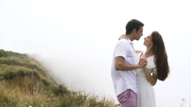 Gelin ve damat, balayı sırasında bulutların tepesindeki dağlarda birbirlerine aşık bir çift olarak poz veriyorlar. Başla. Tatlı ve şefkatli kadın ve erkek sisin önünde.