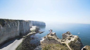 Uçurumun kenarında sarılan çift mavi bulutlu arka planda. Başla. Aşk ve seyahat, mutlu duygular, yaşam tarzı konsepti, yaz mevsiminde nefes kesici deniz manzarası.