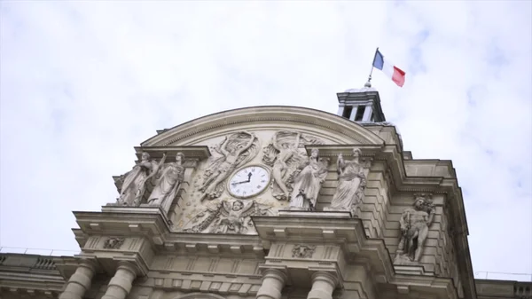 Bandiera francese sventola nel vento su un edificio storico, concetto di architettura. Azione. Vista in basso di un bellissimo vecchio edificio con sculture e orologio . — Foto Stock