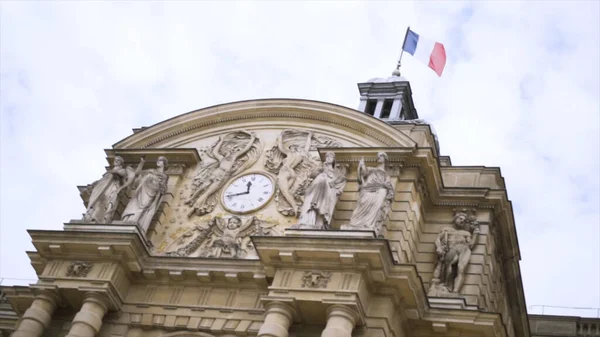 Bandiera francese sventola nel vento su un edificio storico, concetto di architettura. Azione. Vista in basso di un bellissimo vecchio edificio con sculture e orologio . — Foto Stock