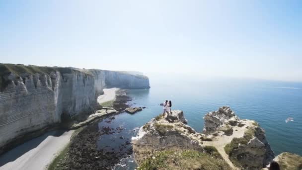 Pareja abrazándose en el borde del acantilado sobre fondo azul cielo nublado. Acción. Amor y viajes, emociones felices, concepto de estilo de vida, paisajes marinos impresionantes en un verano . — Vídeo de stock