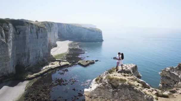 Uomo e donna innamorati sullo sfondo delle montagne e della costa del mare. Azione. Bellissimo paesaggio di riva al mare, tenera coppia appena sposata baciare e abbracciare . — Video Stock