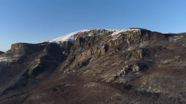 Luchtfoto van bergen op een zonnige herfstdag op een blauwe heldere hemel achtergrond. Neergeschoten. Vliegen over besneeuwde steile rotsachtige muren met groeiende kale bomen. — Stockvideo