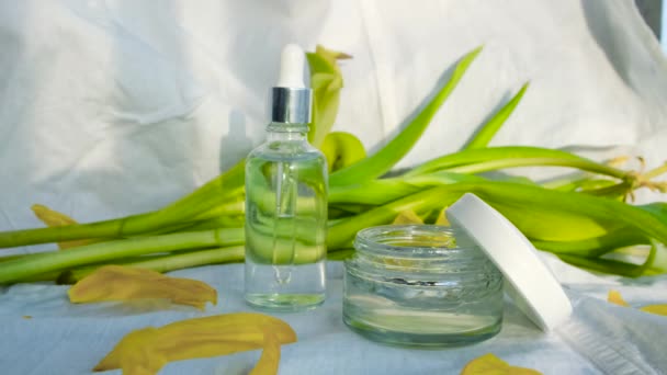 Set de cosméticos para el cuidado facial sobre fondo blanco con flores. Concepto. Suero hidratante y crema para el cuidado de la cara en el fondo de colores delicados — Vídeos de Stock