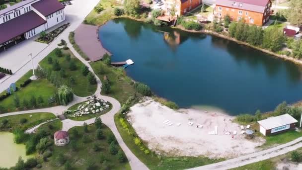 Vista aérea del pequeño pueblo con hermosas cabañas, pequeño lago o estanque y césped verde. Acción. Concepto de vida en la zona ecológica o en el campo . — Vídeos de Stock