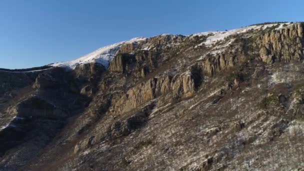 Antenne von schneebedeckten Hügeln mit wachsenden Bäumen an den Hängen vor blauem Himmel Hintergrund. Schuss. Kamera entfernt sich von schönen Felsen, natürlichem Hintergrund. — Stockvideo