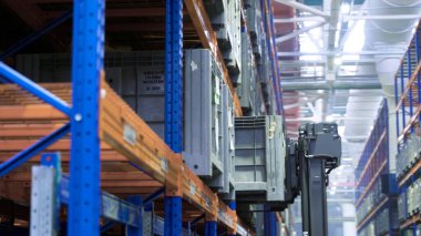 Fabrika deposunda çalışıyorum. Sahne. Şirket ambarındaki raflara konteynır koyma teknolojisi. Otomatik aygıt ağır yükü kaldırır ve deponun rafına yerleştirir.