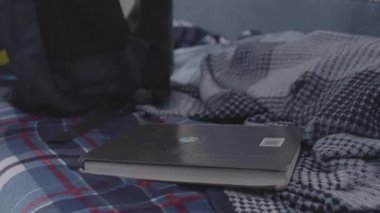 Yataktan ders kitabını alıp sırt çantasına koyan bir çocuğun yan görüntüsü. Stok görüntüleri. Genç çocuk okul için sırt çantasını hazırlıyor, eğitim konsepti..