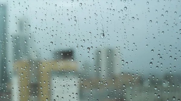 Zamknij okno w deszczowy dzień z dużymi kroplami na zamazanym mieście ang szare ciężkie tło nieba. Materiał filmowy. Przezroczyste krople wody na pionowej powierzchni szkła. — Zdjęcie stockowe