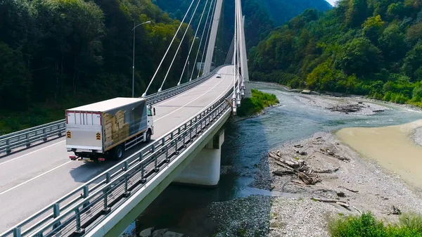 A teherautó nyáron átkel a gyönyörű hídon. Jelenet. Top kilátás teherautó szállító dolgokat áthajt híd hátterében gyönyörű erdős táj. Utazás és áthelyezés — Stock Fotó