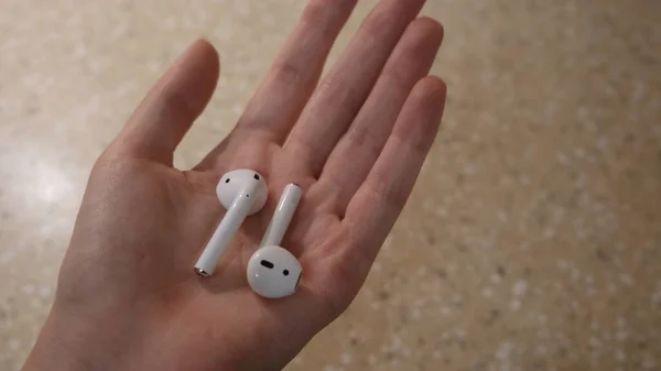Modern airpods headphones in the hand of a young woman. Concept. Amazing music technology in the hand of a girl — Stock Photo, Image