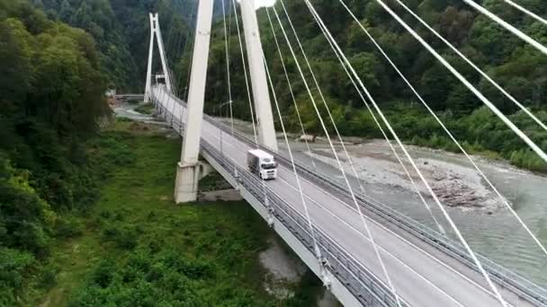 Aerial view of new concrete bridge with highway and driving white truck, transportation of goods concept. Stock footage. White lorry moving along green forest, view from above. — Stock Video