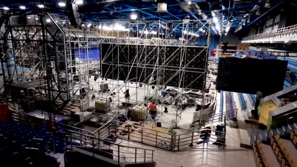 Installatie van podium met apparatuur voor concert in het stadion. Voorraadbeelden. Werknemers installeren enorme apparatuur en schijnwerpers voor het podium in indoor stadion voor concert — Stockvideo