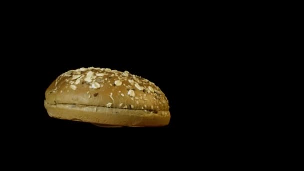 Primer plano del bollo de hamburguesa giratorio en fuego aislado sobre fondo negro. Imágenes de archivo. Sabroso bollo de hamburguesa fresca con fuego durante el proceso de cocción, comida y concepto de cocina . — Vídeo de stock